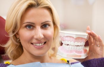 A satisfied woman with a perfect smile sitting in a dental chair and showing a dental model.